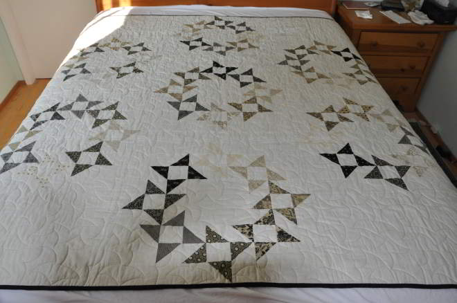 A quilt of starry circles in mostly blacks & greys on an off white background.
