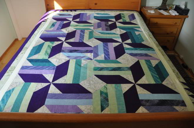 Quilt in purples, blues and greens in star pattern blocks, called 'Twirling'.